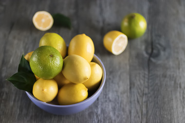 Fresh ripe lemons and limes in blue bowl on gray wooden table.