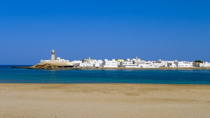 View of the town of Sur, Oman, with whitewashed buildings and lighthouse extending into the blue waters