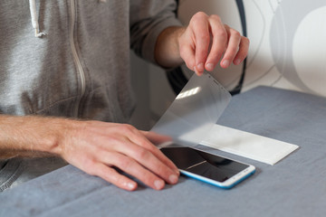 Renovation, repair concept. Preparing the screen for gluing new accessory 3d protective glass. High angle top side profile view man removes the matte protective film on the digital device or phone