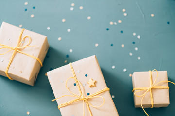 handcrafted present. gifts wrapped in craft paper and tied with yellow twine. festive boxes on blue background with confetti decor. holiday celebration and congratulation.