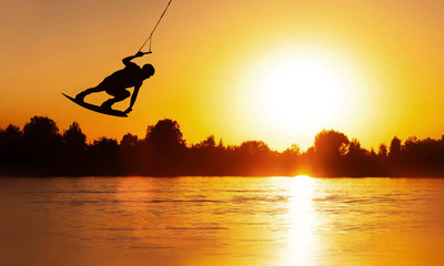 Wake Board a man does a trick at sunset on the Board on the water splashes