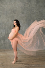 Fototapeta na wymiar beautiful young pregnant woman wrapped into pink fabric in studio