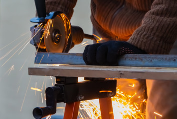 A man in the black working gloves cuts metal using an angle grinder tool with beautiful yellow...