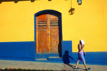 LEON, NICARAGUA - DEC 2015: A woman covers her face from the sun while walking past brightly coloured buildings in the colonial city of León in northern Nicaragua