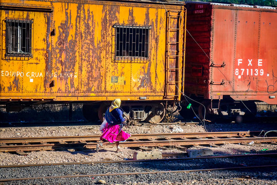 CREEL, MEXICO-Jan 2016: A native Raramuri woman in bright clothing runs across railway tracks while waiting for the El Chepe Copper Canyon train at Creel railway station in Chihuahua, northern Mexico