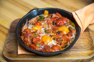 Shakshuka - eggs in tomato sauce in a skillet over wooden background.