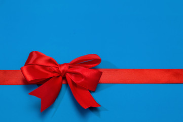 Red bow on a blue background, silk ribbon, empty space for text.
