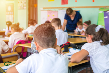 group of school kids sitting and listening to teacher in classroom from back