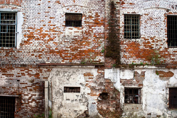 Fototapeta na wymiar Prison in Siberia – an abandoned unrepaired building of the old prison in Tobolsk: red brick texture on a white wall, Windows in bars