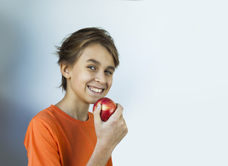 Young boy in orange t-shirt eating a red apple