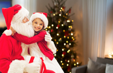 Fototapeta na wymiar holidays, childhood and people concept - smiling girl hugging santa claus with gift over christmas tree at home background
