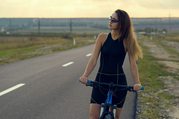 A girl riding a mountain bike on an asphalt road, beautiful portrait of a cyclist at sunset	