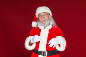 Christmas. Serious Santa Claus in white gloves adjusts her glasses and stares into the camera. Isolated on red background.