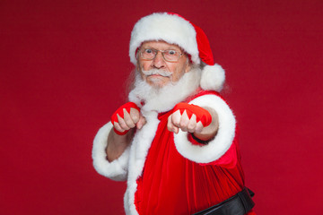 Christmas. Santa Claus with red bandages wound on his hands for boxing imitates kicks. Kickboxing, karate, boxing. Isolated on red background.