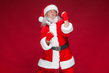 Christmas. Santa Claus with red bandages wound on his hands for boxing imitates kicks. Kickboxing, karate, boxing. Isolated on red background.