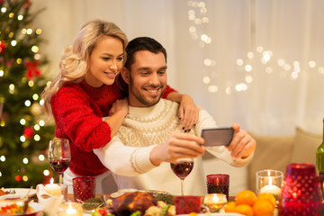 christmas, holidays, technology and people concept - happy couple in taking selfie by smartphone at home dinner