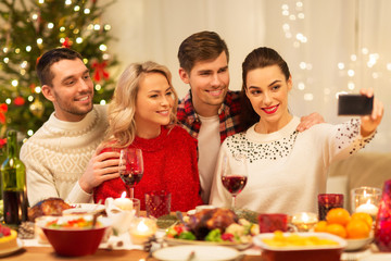 holidays and celebration concept - happy friends taking selfie by smartphone at home christmas dinner