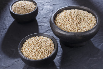 Quinoa grains with spoon and bowl on black background