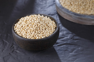 Quinoa grains with spoon and bowl on black background