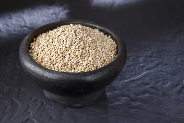 Quinoa grains with spoon and bowl on black background