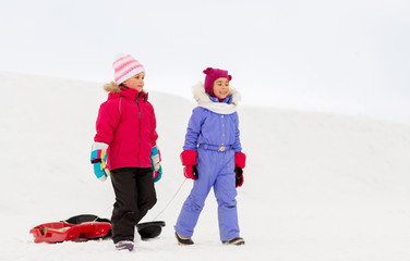 childhood, sledging and season concept - happy little girls with sleds walking in winter