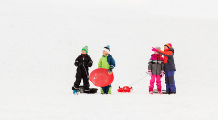 childhood, sledging and season concept - group of happy little kids with sleds in winter