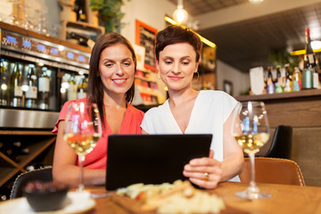 leisure, technology and lifestyle concept - happy women with tablet pc computer at wine bar or restaurant