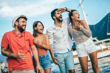 Friends walking by the harbor of a touristic sea resort with boats on background