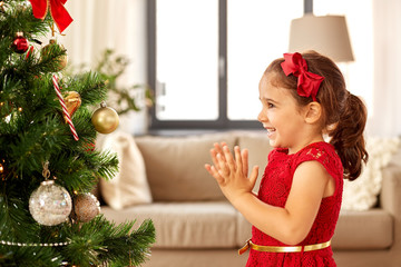 winter holidays and people concept - happy little girl decorating christmas tree at home