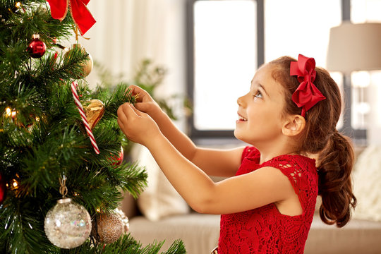 winter holidays and people concept - happy little girl decorating christmas tree at home