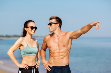 fitness, sport and lifestyle concept - happy couple in sports clothes and sunglasses on beach