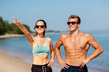 fitness, sport and lifestyle concept - happy couple in sports clothes and sunglasses on beach