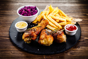 Grilled drumsticks with french fries and vegetables on wooden background