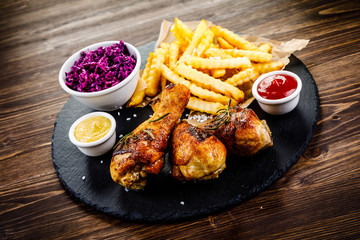Grilled drumsticks with french fries and vegetables on wooden background