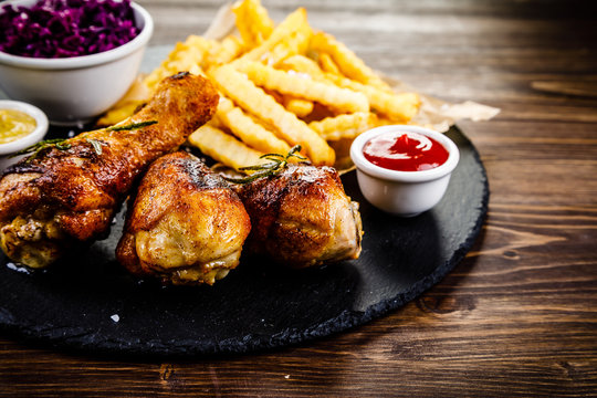 Grilled drumsticks with french fries and vegetables on wooden background