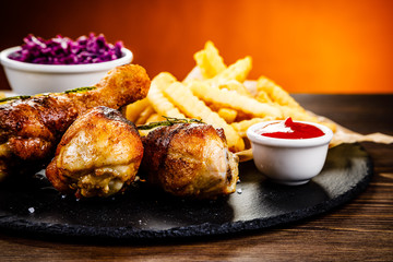 Grilled drumsticks with french fries and vegetables on wooden background