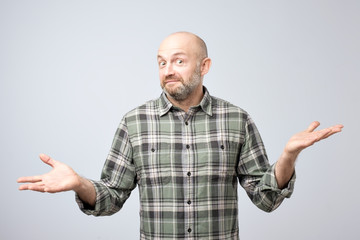 Portrait of confused mature man d standing over white background gesturing with hands.
