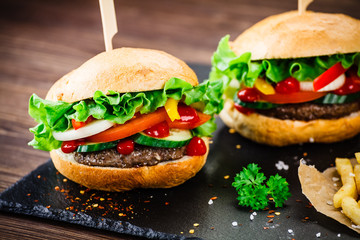 Tasty hamburgers with french fries served on fashionable black stone plate