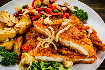 Fried pork chop with potatoes and vegetable salad on wooden background