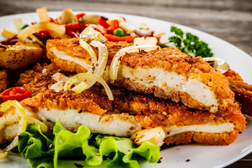 Fried pork chop with potatoes and vegetable salad on wooden background