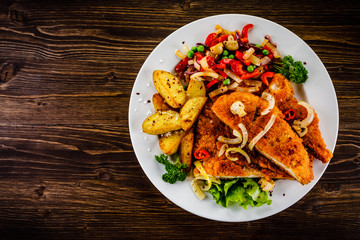 Fried pork chop with potatoes and vegetable salad on wooden background