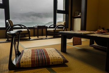 Naklejka premium Tradycyjny pokój w ryokanie - japoński hotel, z niskimi krzesłami i stolikami z przodu zdjęcia i oknem w tle. Mgliste góry to widok z okna.