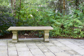 Solitary white stone bench on a white brick patio with lush green foliage in the background
