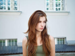Art portrait of a young pretty redhead woman posing outdoors in green dress against city building background