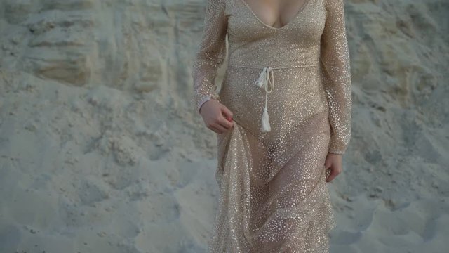 long female legs go along the dune in the sand. the woman gently tramples the sand. a long golden dress develops in the wind. 4K