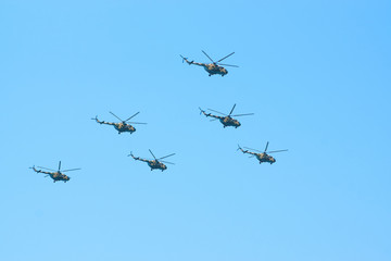 Fototapeta na wymiar Military helicopters maneuvers in the blue sky. Group combat helicopters in flight during a military demonstration