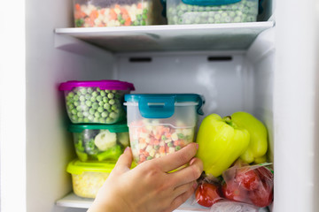 Woman taking container with frozen mixed vegetables from refrigerator.
