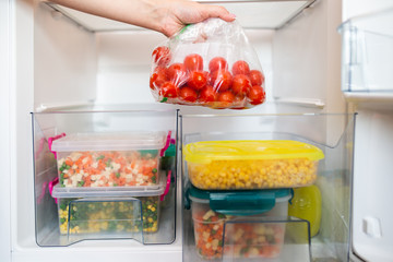Woman putting bag with cherry tomatoes in refrigerator.