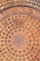 Round circular pattern of squares, rust orange storm drain cover, words storm drain and Made in India
