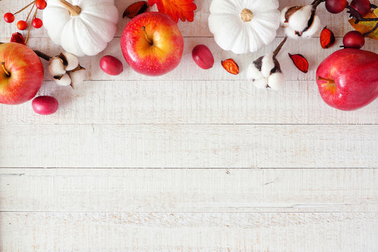 Red and white theme autumn top border with apples and pumpkins on a white wood background. Copy space.
